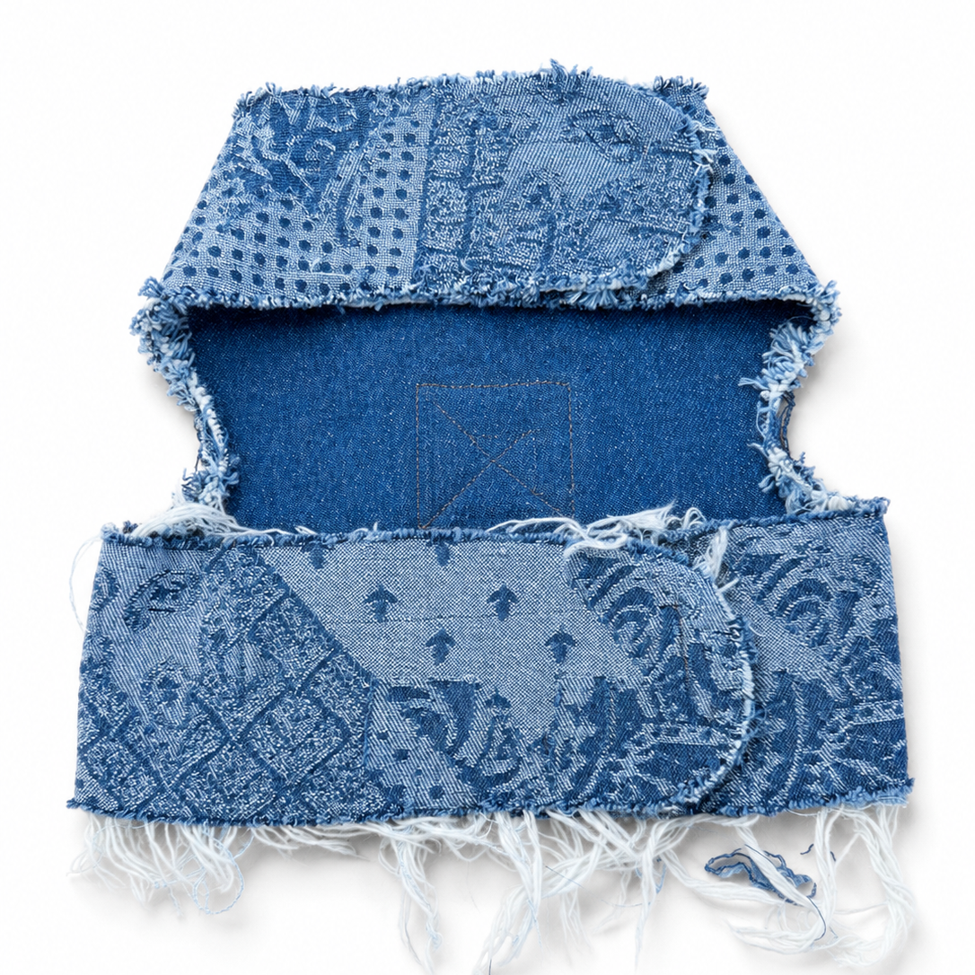A blue denim harness with a distressed, frayed edge and a faded patchwork pattern, displayed flat against a white background.