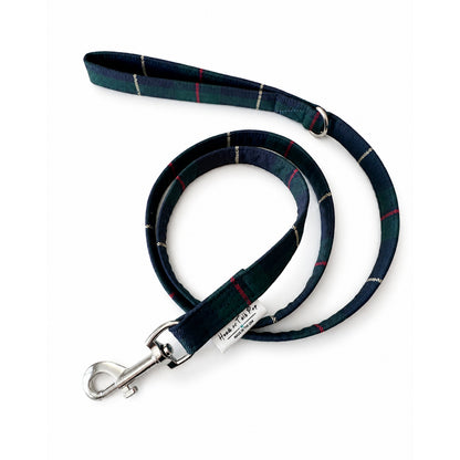 A navy blue tartan plaid dog leash with silver metal hardware and a white brand tag shown on a plain white background.