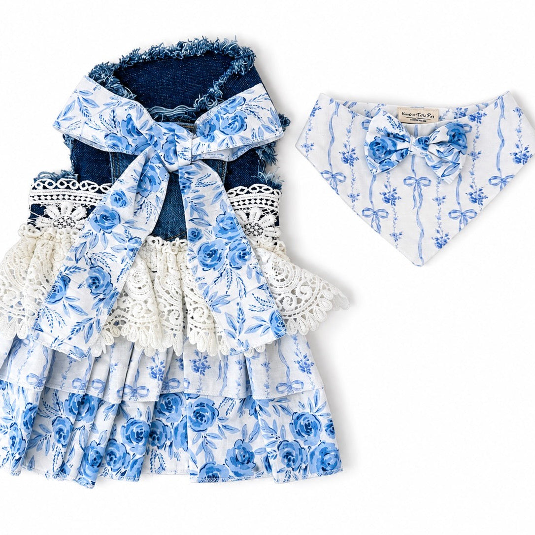 A two-piece pet outfit set featuring a tiered ruffle dress with a blue and white floral print, lace trim, and a dark blue denim lining with a matching bow, accompanied by a matching bandana.