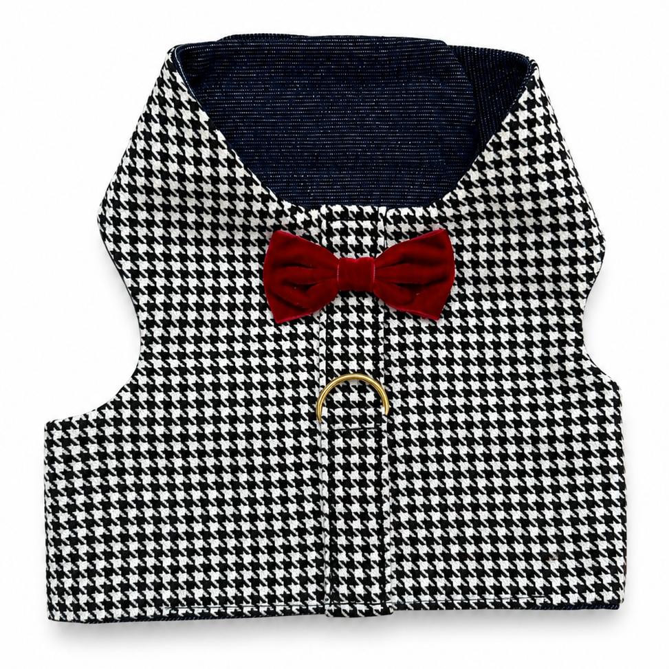 A small black and white houndstooth harness with a dark navy blue lining, a red bow tie, and a gold metal ring on a white background.