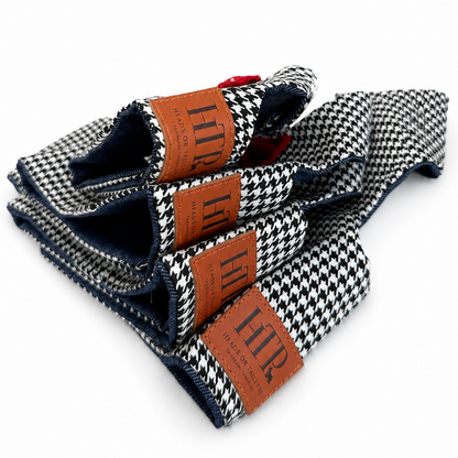 Three folded harnesses with a black and white houndstooth pattern, featuring brown leather brand tags with 'HTP' printed on them, set against a plain white background.