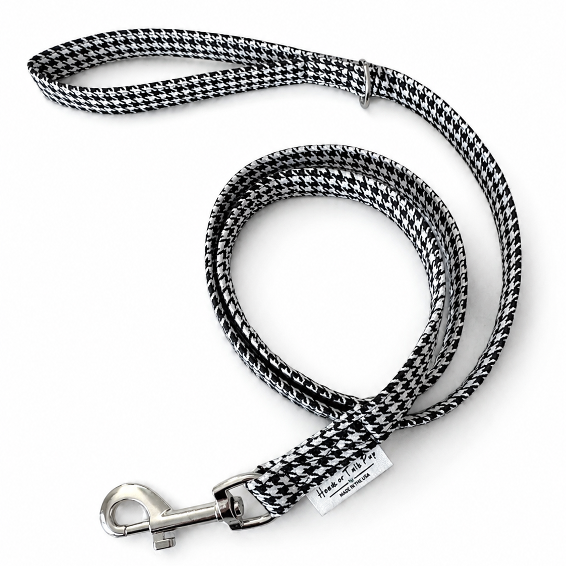 A black and white houndstooth patterned dog leash with a silver metal snap hook and a small white brand tag, displayed on a clean white background.