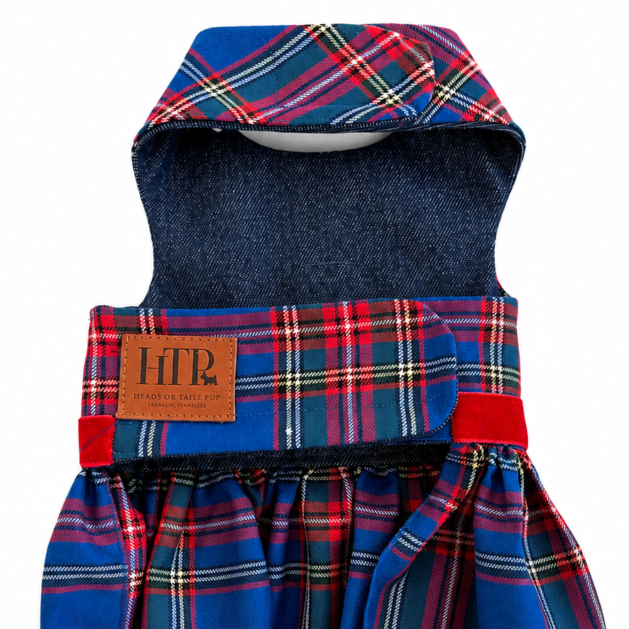 A pet dress with a blue and red plaid pattern, featuring a solid navy blue denim-like inner lining and a brown leather patch on the front with the letters 'HTP'.