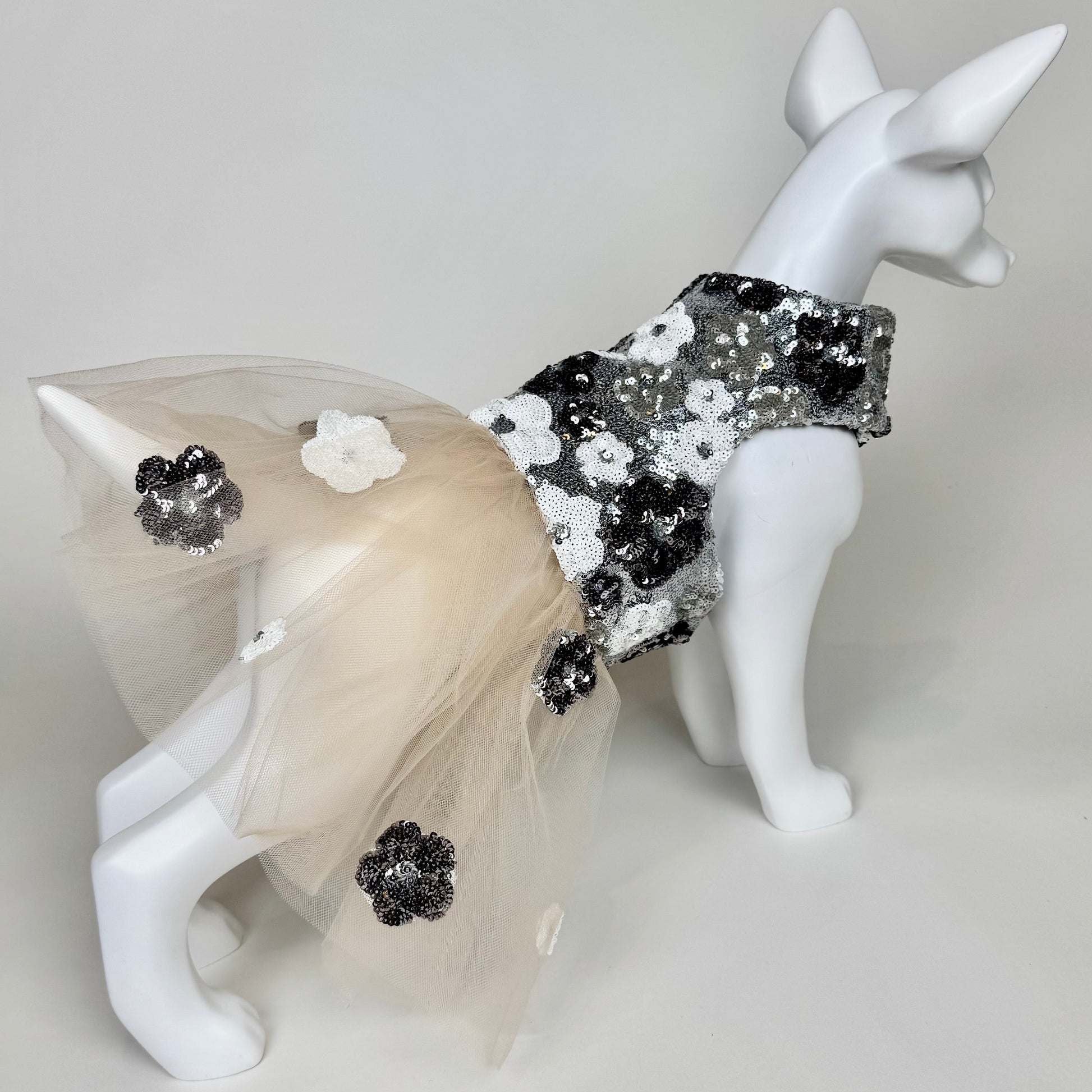Mannequin dog wearing a decorative outfit with flowers and sequins on a light gray background