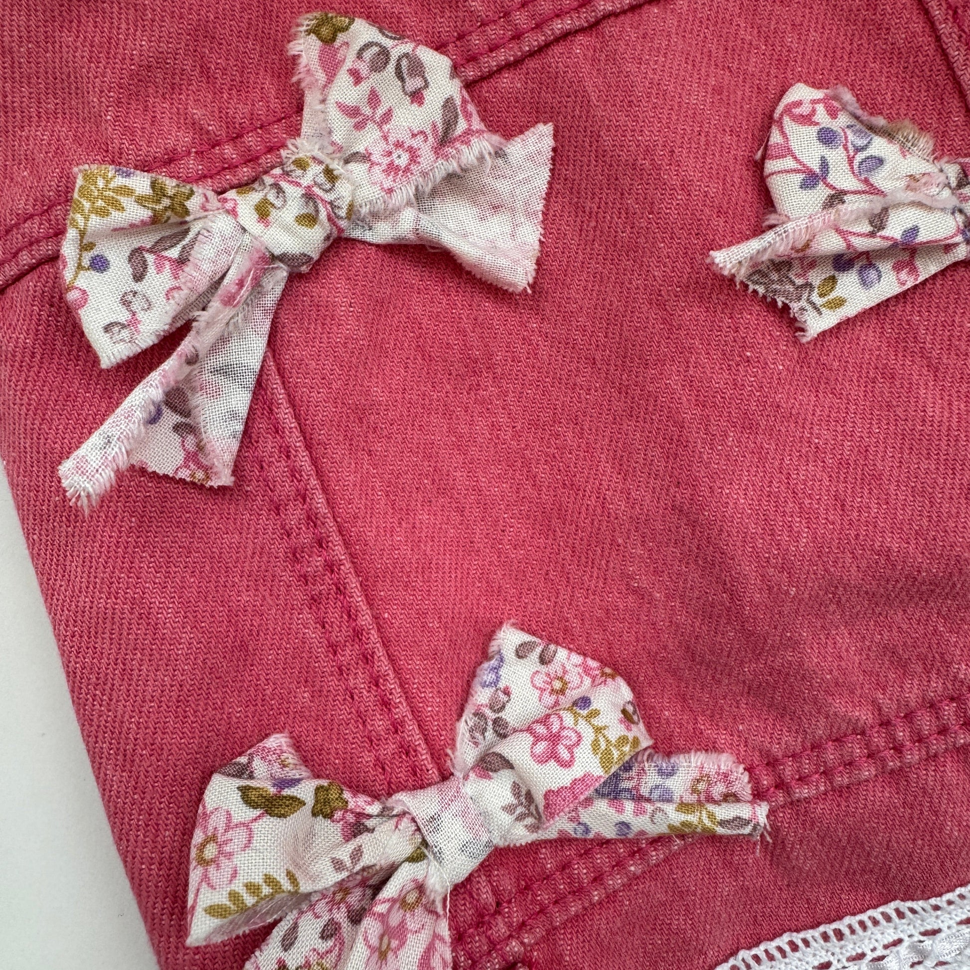 Pink denim jacket with floral fabric bows on a white background