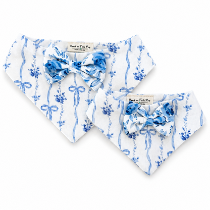 Two white pet bandanas with blue floral and ribbon patterns, each styled with a matching blue bow tie, displayed on a clean white background.