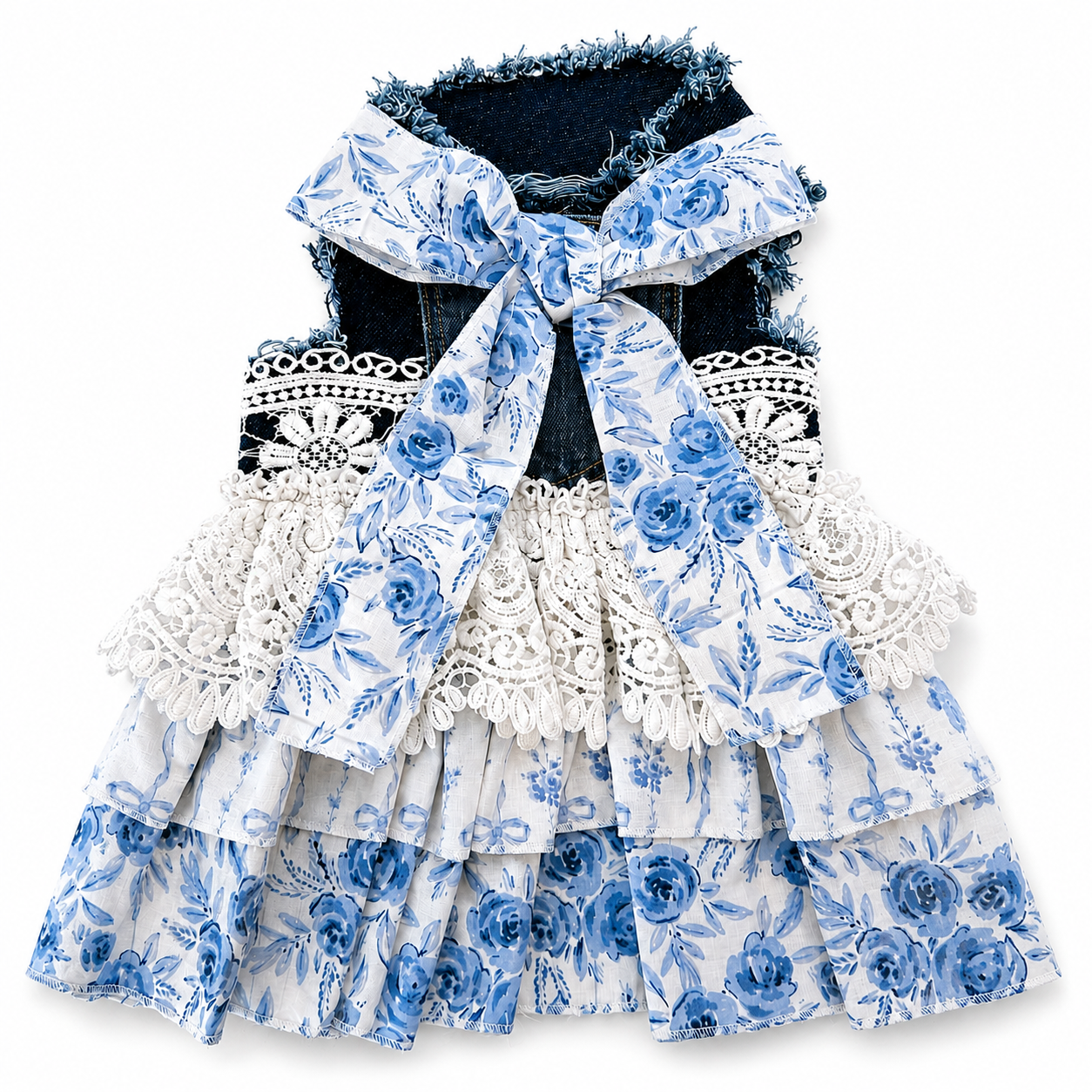 A sleeveless tiered dress for dogs, featuring a blue and white floral print, white lace ruffles, and a large matching fabric bow at the collar over a dark denim backing.