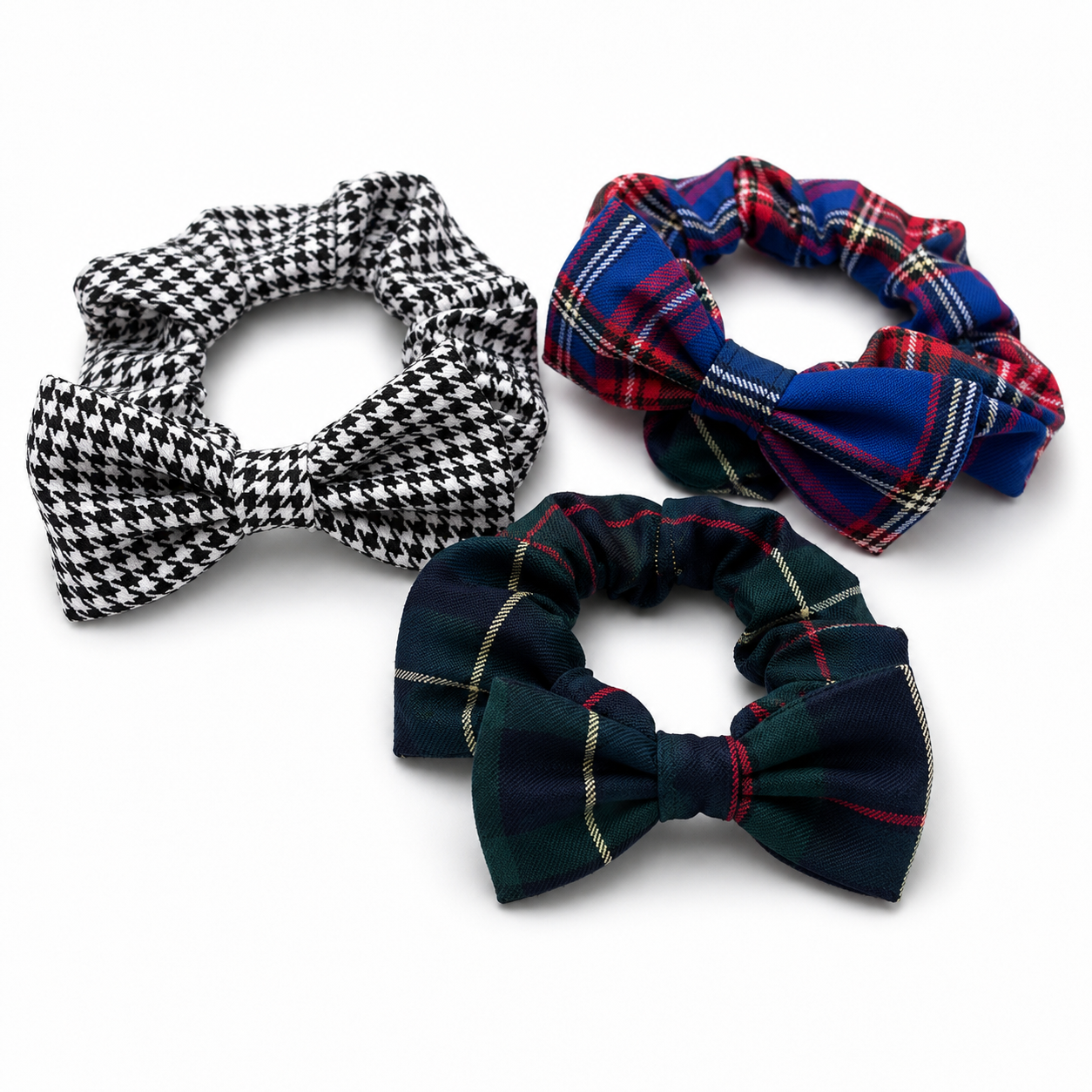 Three fabric pet collar scrunchies with bow details, displayed on a clean white background. The top-left scrunchie features a black and white houndstooth pattern, the top-right scrunchie has a red, blue, and cream tartan plaid pattern, and the bottom scrunchie is a dark green and navy tartan plaid pattern.