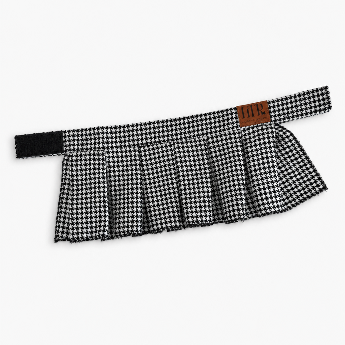 A black and white houndstooth pleated skirt with a wide waistband and a small brown leather brand patch reading 'HTP' on the side, shown against a plain light gray background.