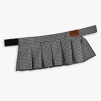 A black and white houndstooth pleated skirt with a wide waistband and a small brown leather brand patch reading 'HTP' on the side, shown against a plain light gray background.
