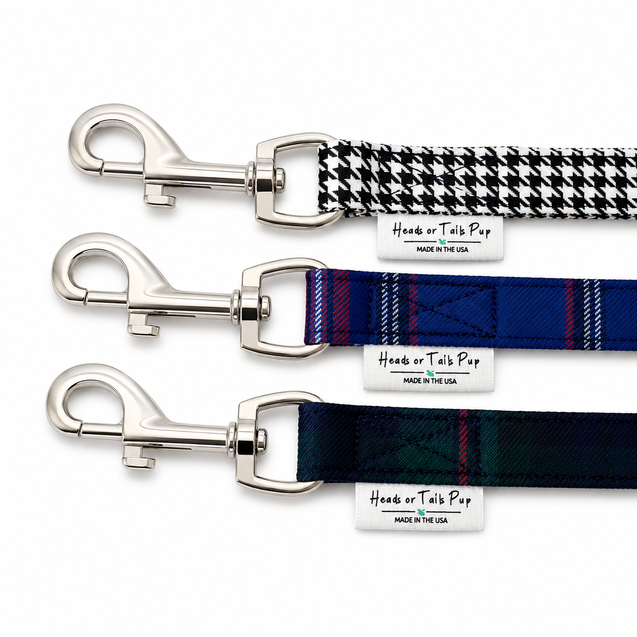 Three dog leashes with silver metal clamps arranged diagonally on a white background. The top leash has a black and white houndstooth pattern, the middle leash has a blue and red plaid pattern, and the bottom leash has a dark green and blue plaid pattern.
