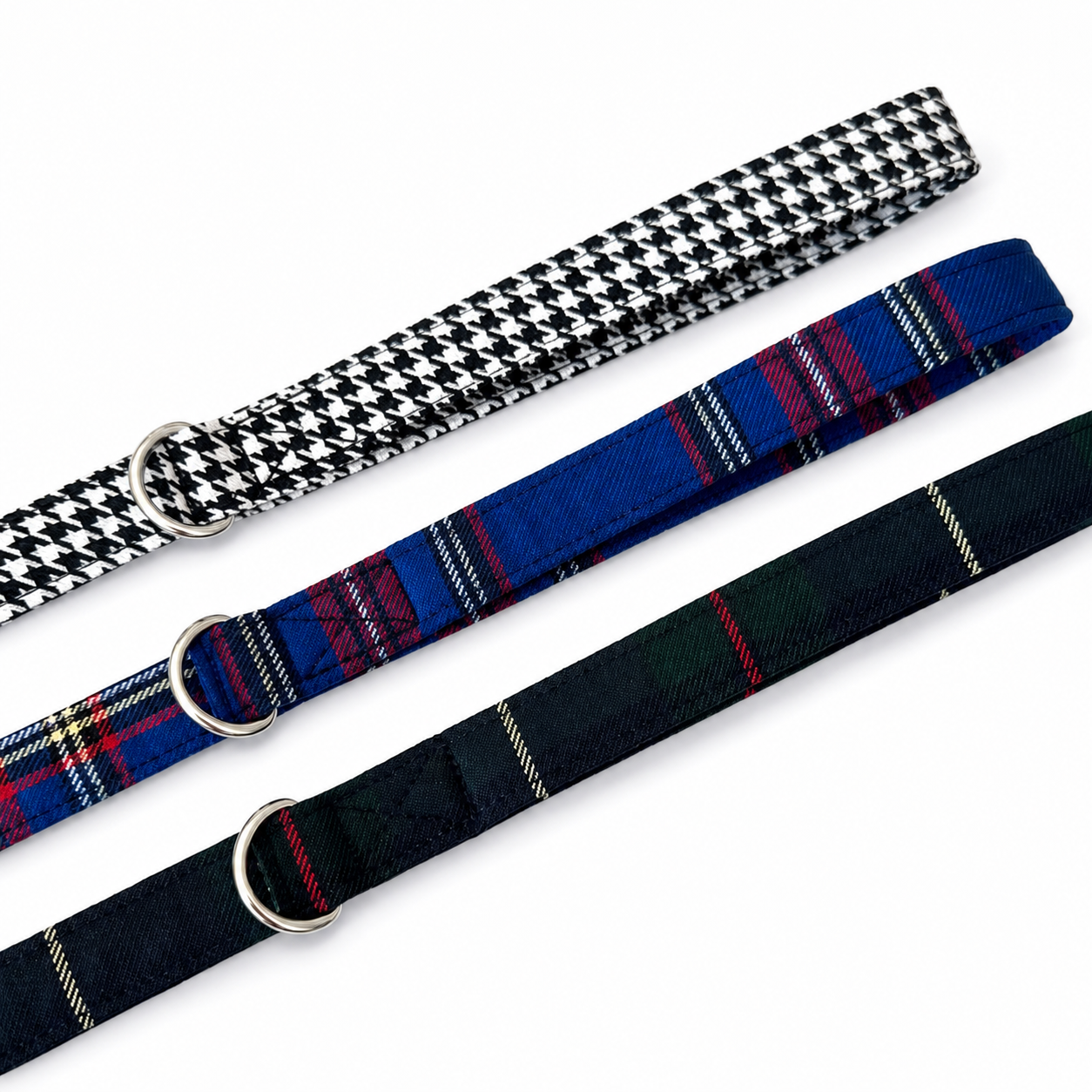Three woven pet collars with silver metal rings, arranged diagonally on a white background. The top collar has a black and white houndstooth pattern, the middle collar has a blue tartan plaid pattern with red and yellow stripes, and the bottom collar has a dark green and black tartan plaid pattern with red and yellow stripes.