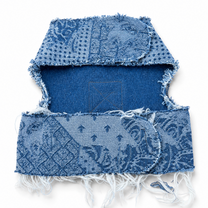 A blue denim harness with a distressed, frayed edge and a faded patchwork pattern, displayed flat against a white background.